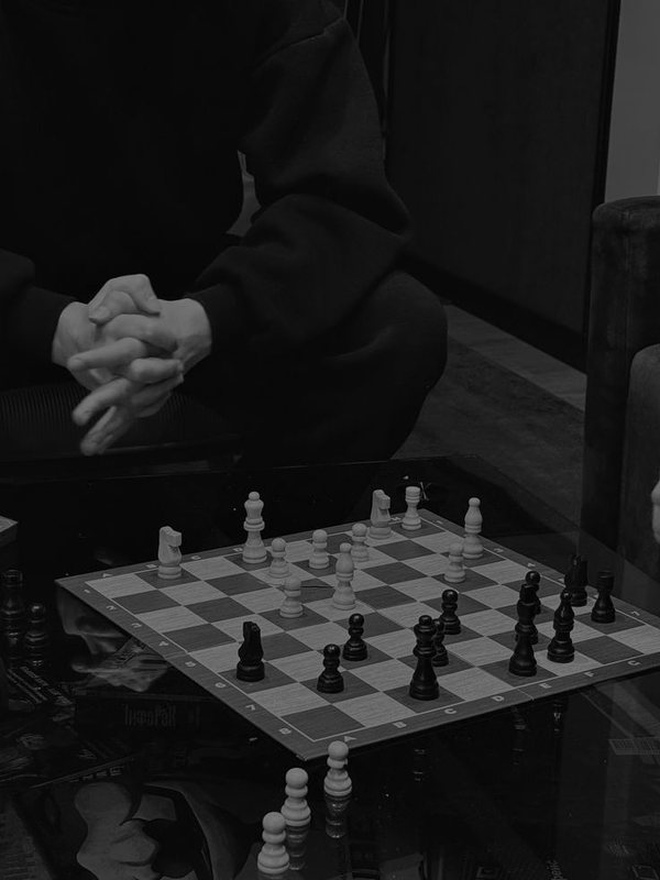 Tablero de ajedrez con una persona sentada frente a él, en blanco y negro